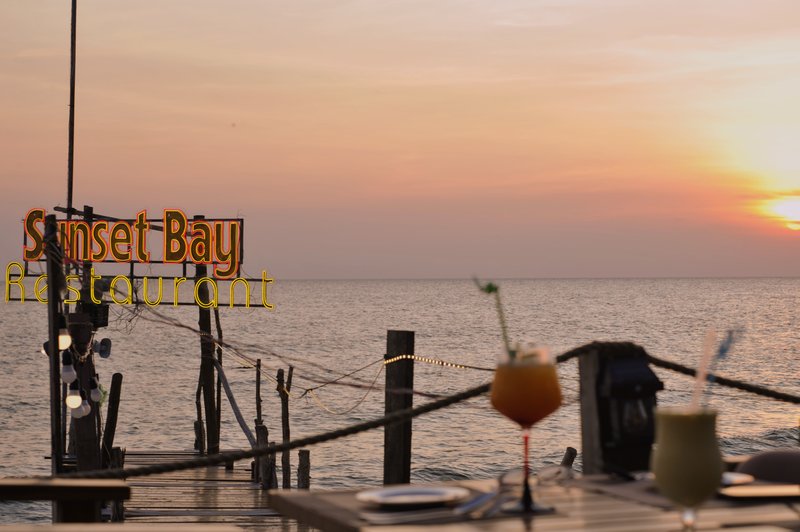 Sunset cocktails with neon sign and ocean backdrop