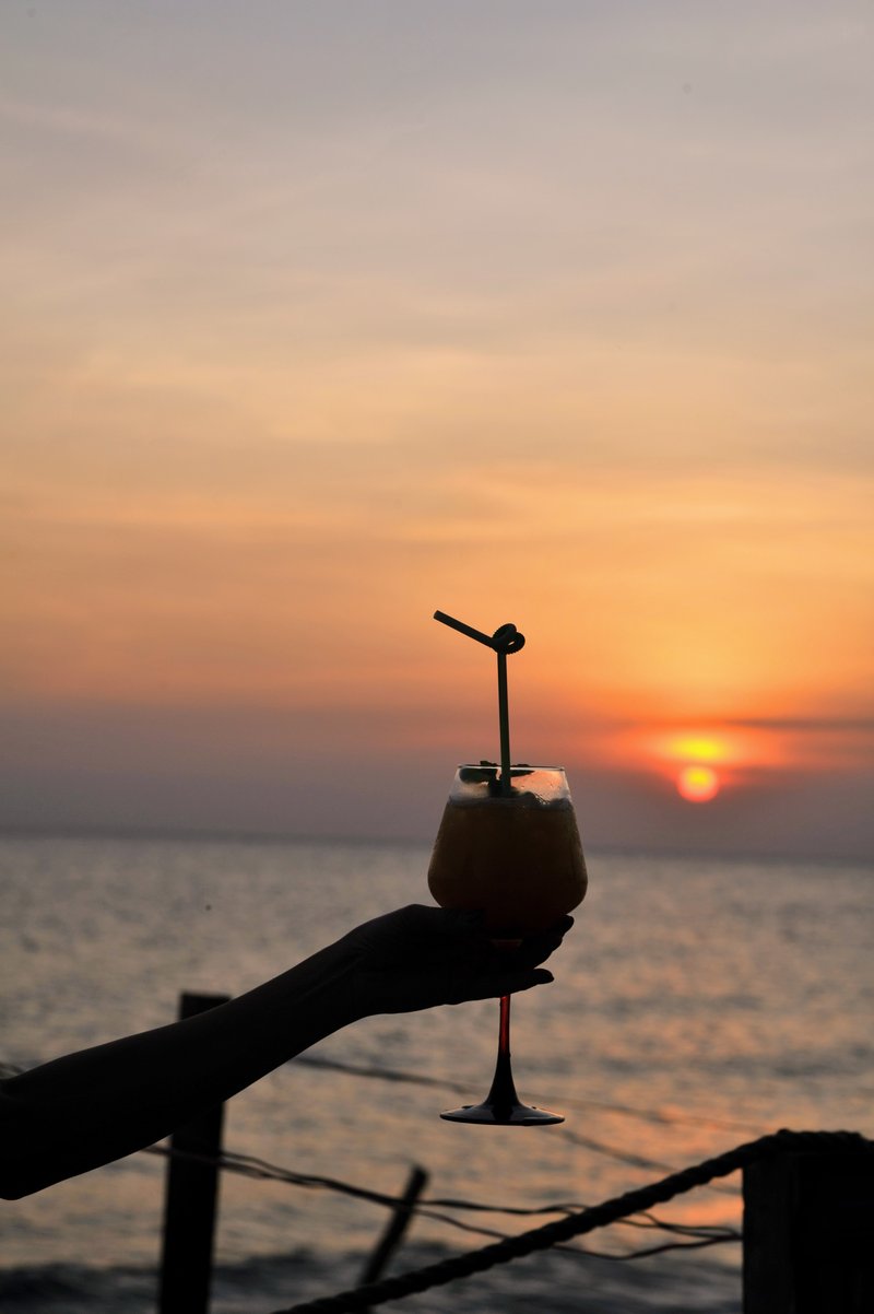 Hand holding cocktail silhouetted against sunset sky