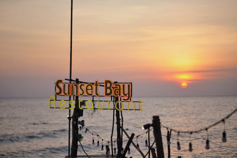 Neon Sunset Bay sign glowing at pastel sunset