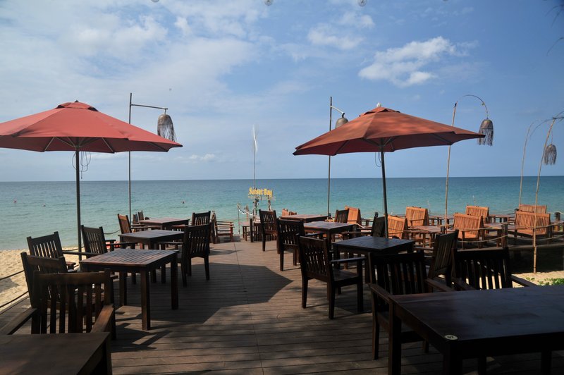 Beachfront deck dining area with red parasols and turquoise ocean